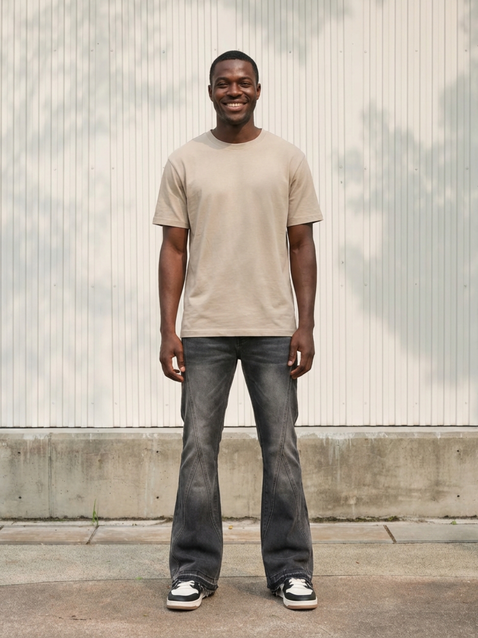 Homme portant un t-shirt beige avec un jean flare gris délavé, sur fond clair