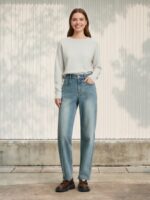 Femme portant un pull beige avec un jean mom délavé taille haute, sur fond clair
