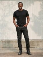 Homme portant un t-shirt noir avec un jean de moto noir, sur fond beige