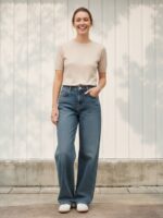 Femme portant un t-shirt beige avec un jean regular bleu vintage, sur fond beige