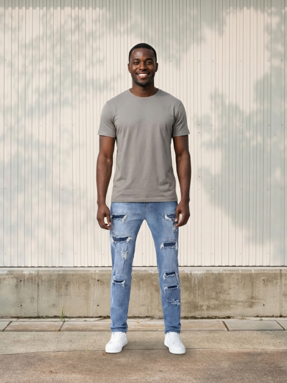 Homme portant un t-shirt taupe avec un jean skinny bleu clair déchiré, sur fond beige