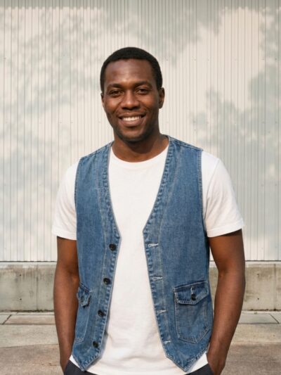 Homme portant une veste en jean sans manche façon veston, sur fond beige