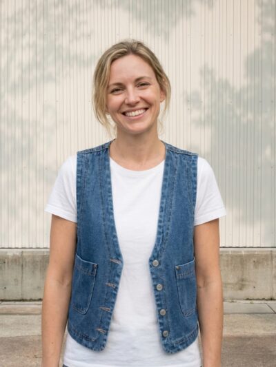 Femme portant un t-shirt blanc avec une veste sans manche en jean bleu façon veston, sur fond beige