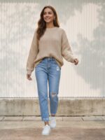 Femme portant un jean droit bleu clair 7/8 avec déchirures, dévoilant les chevilles pour un style urbain avec baskets blanches sur fond clair extérieur.