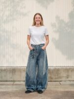 Femme portant un t-shirt blanc avec un jean baggy au style sportswear avec des rayures, sur fond clair