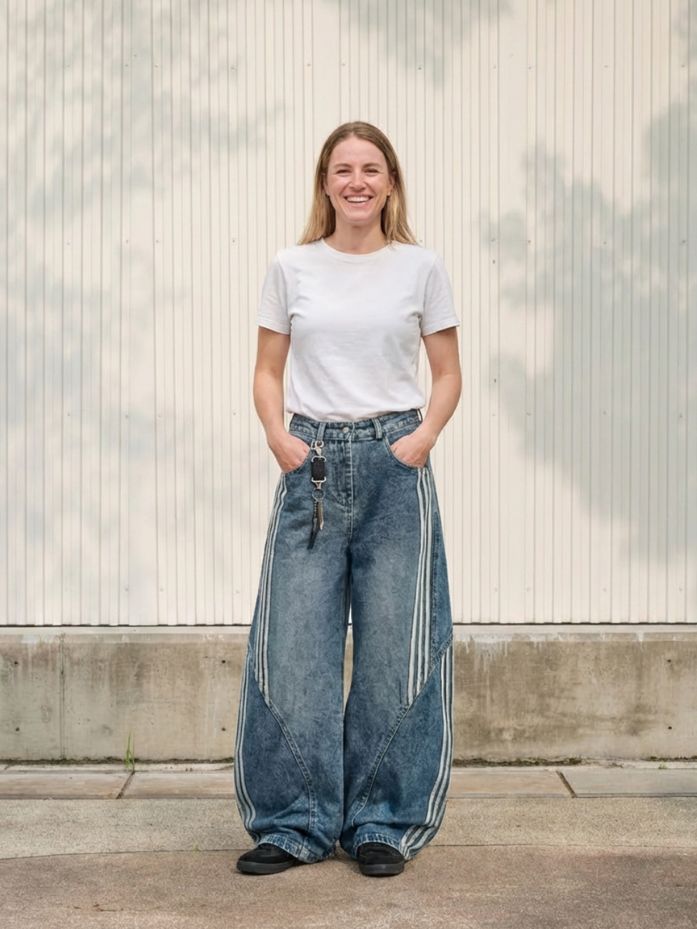 Femme portant un t-shirt blanc avec un jean baggy au style sportswear avec des rayures, sur fond clair