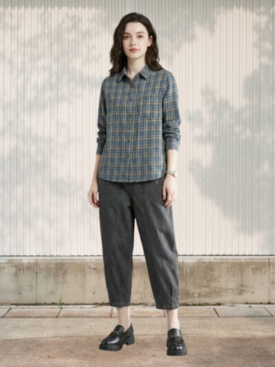 Femme debout portant le Jean 7/8 femme design ample à poches marquées : coupe large, tissu gris foncé, poches visibles, chemise à carreaux et mocassins noirs.