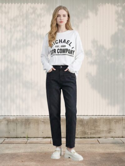 Femme portant un jean 7/8 droit à taille haute gris anthracite avec un sweatshirt blanc et des baskets beiges claires dans un lieu éclairé.