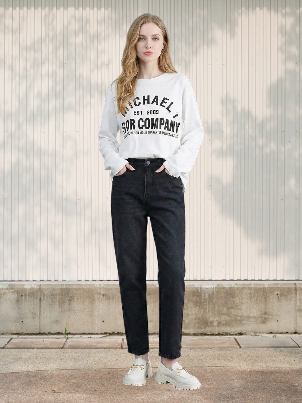 Femme portant un jean 7/8 droit à taille haute gris anthracite avec un sweatshirt blanc et des baskets beiges claires dans un lieu éclairé.