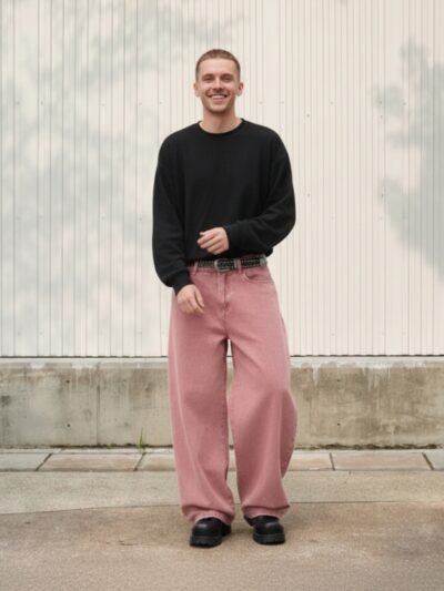 Homme portant un pull noir avec un jean baggy rose, sur fond beige