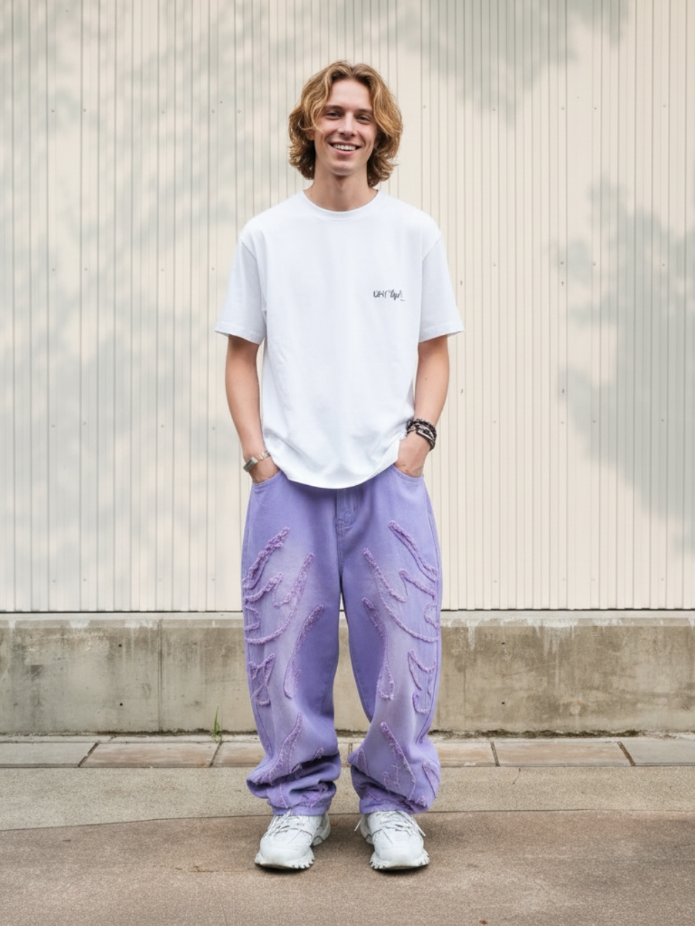 Homme portant un t-shirt blanc avec un jean baggy violet pastel, sur fond clair
