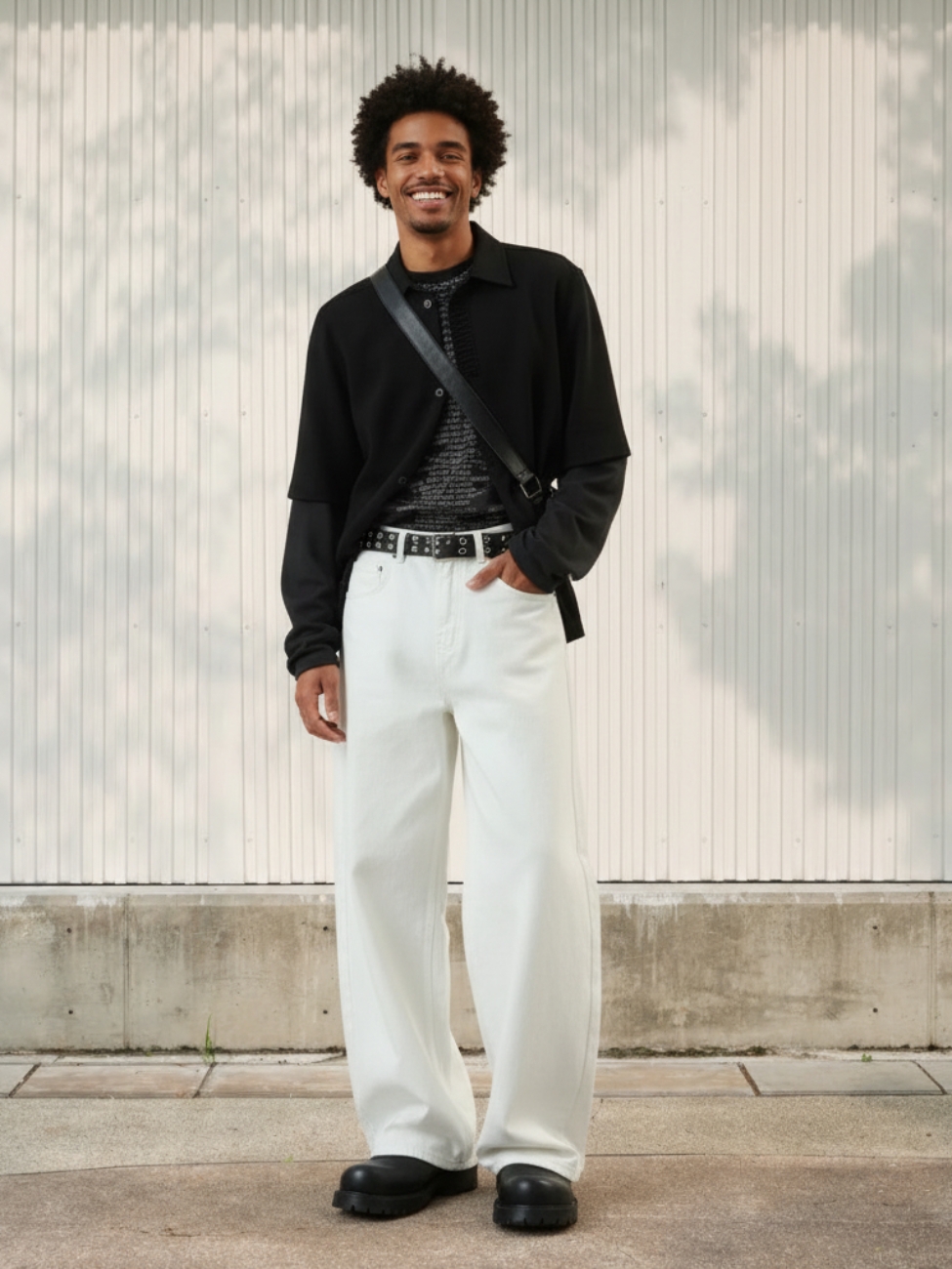Homme portant une veste noire avec un jean blanc à coupe loose, sur fond beige