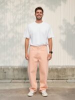 Homme portant un t-shirt blanc avec un jean loose rose corail, sur fond beige