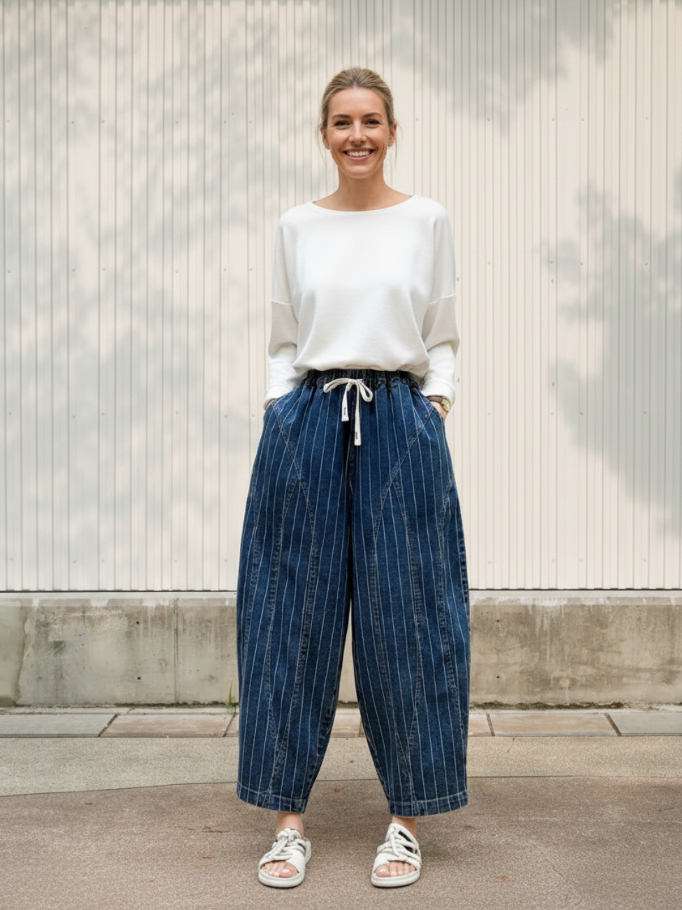 Femme portant un haut blanc avec un jean bleu foncé rayé à coupe ballon, sur fond beige