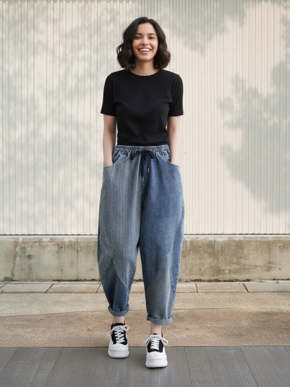 Femme portant un t-shirt noir avec un jean rayé à coupe ballon, sur fond beige