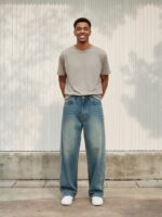 Homme portant un t-shirt gris avec un jean rayé délavé bleu vintage, sur fond beige