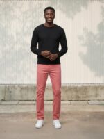 Homme portant un pull noir avec un jean slim rose, sur fond beige