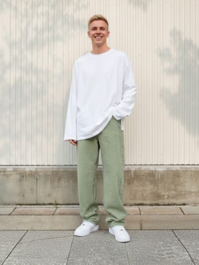 Homme portant un pull blanc avec un jean baggy vert, sur fond beige