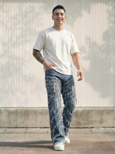 Jean moto homme bleu destroyed bandages vintage large porté par un homme, coupe droite ample, denim bleu délavé, déchirures visibles, bandages décoratifs, style streetwear rétro affirmé.