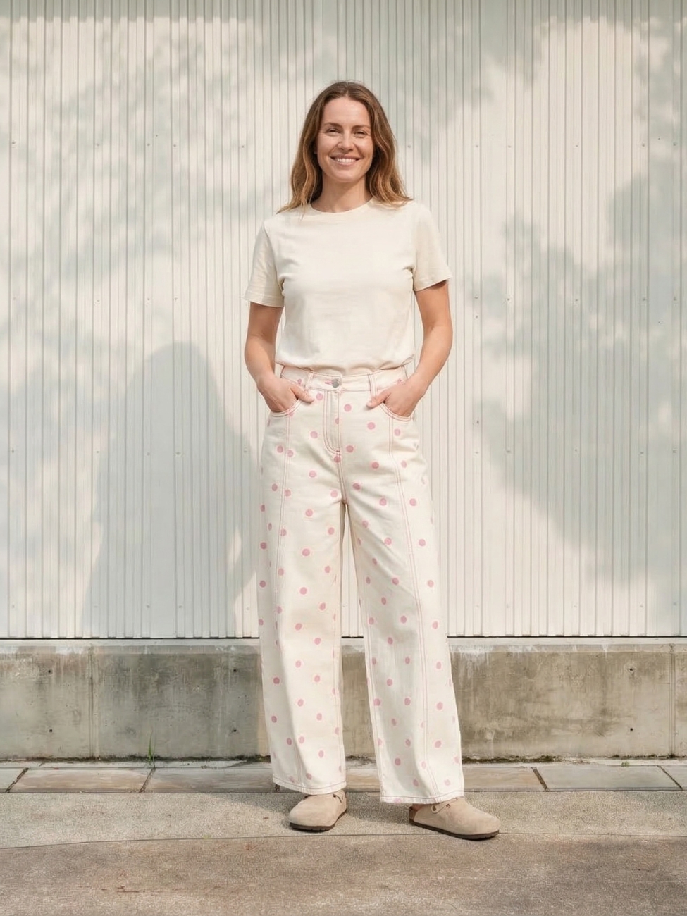 Femme portant un t-shirt blanc avec un jean barrel blanc à pois roses, sur fond beige