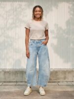Femme portant un t-shirt beige avec un jean barrel délavé bleu clair, sur fond beige