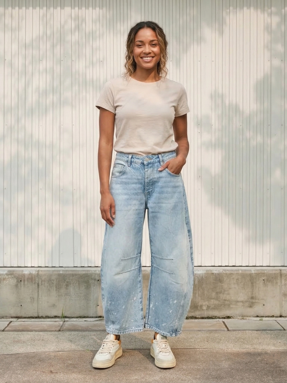 Femme portant un t-shirt beige avec un jean barrel délavé bleu clair, sur fond beige