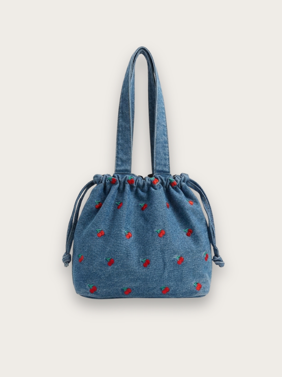 Sac à main en jean bleu brodé cerise à porter sur l'épaule, format sceau, sur fond gris