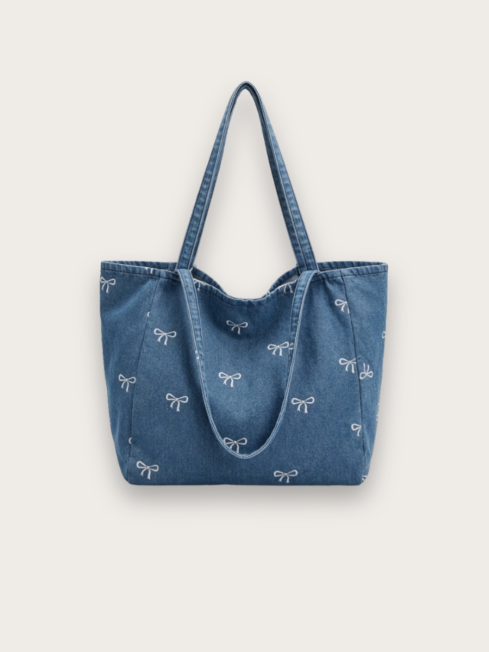 Sac en jean porté épaule style tote bag de couleur bleu avec des noeuds brodés, sur fond gris