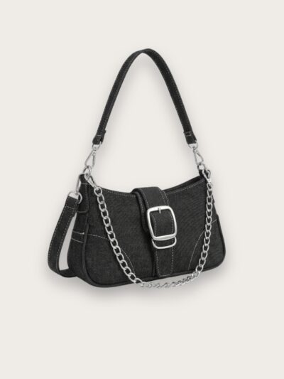 Sac à main en jean noir porté épaule format baguette avec une chaîne argentée, sur fond gris